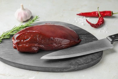 Photo of Piece of raw beef liver and knife on light table, closeup