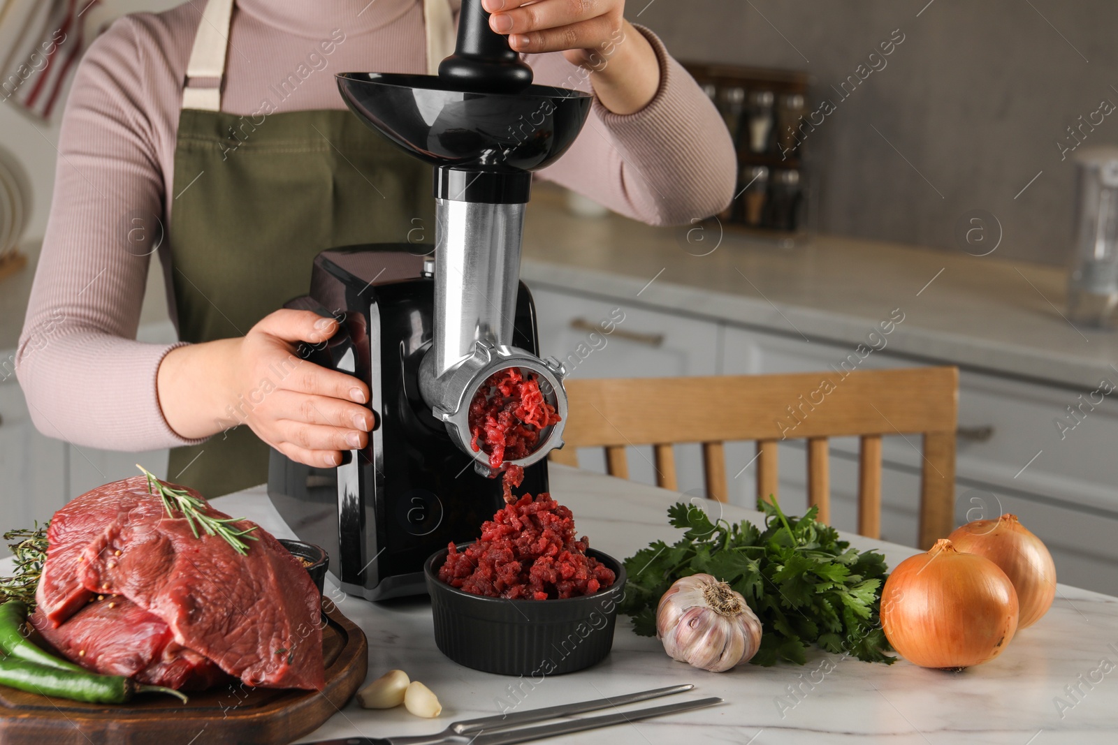 Photo of Woman making beef mince with electric meat grinder at white marble table in kitchen, closeup