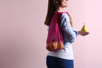Photo of Woman holding net bag with fresh ripe pears on pink background, closeup