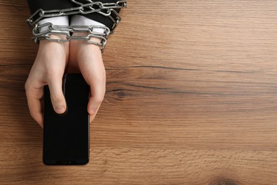 Photo of Man holding smartphone in chained hands at wooden table, top view. Internet addiction