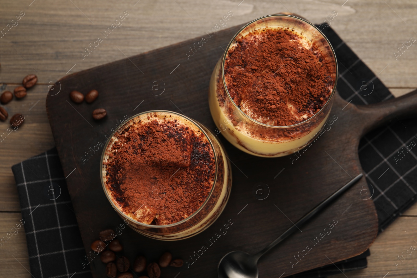 Photo of Delicious tiramisu in glasses, spoon and coffee beans on wooden table, top view