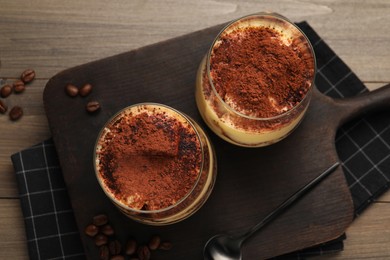 Photo of Delicious tiramisu in glasses, spoon and coffee beans on wooden table, top view