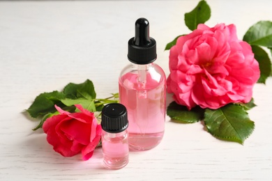 Photo of Fresh flowers and bottles of rose essential oil on white table