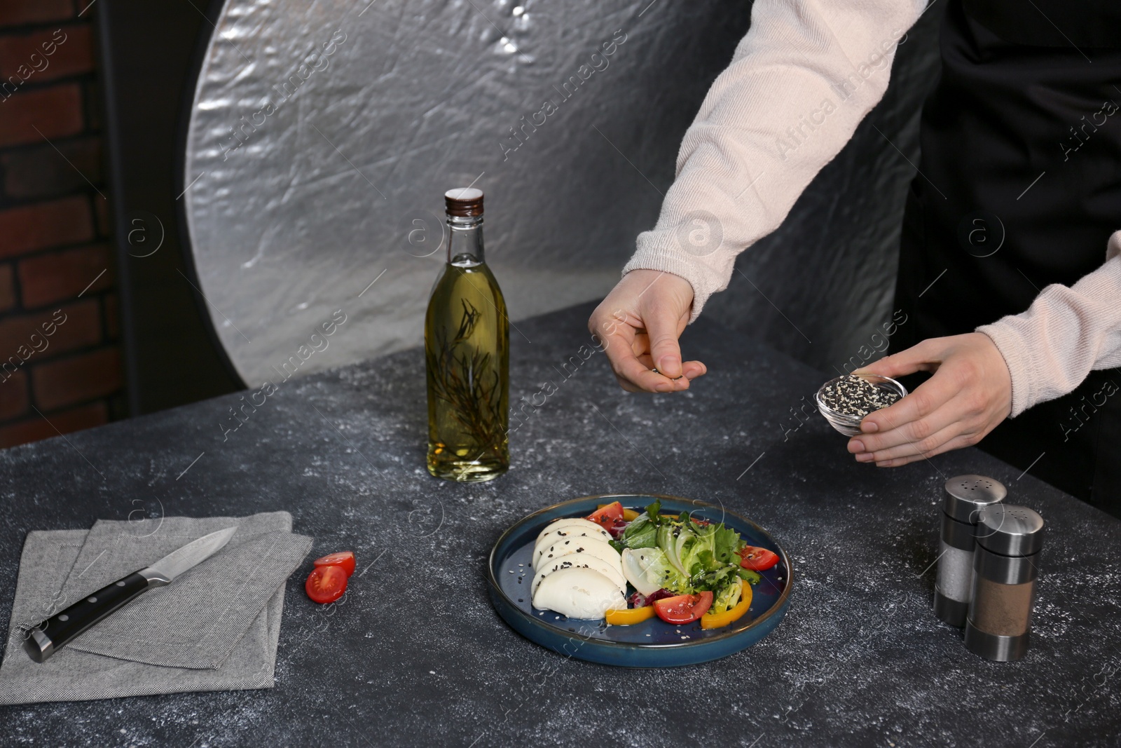 Photo of Food stylist preparing delicious salad with mozzarella and tomatoes for photoshoot at dark grey table in studio, closeup