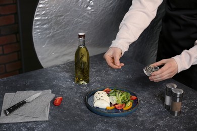 Food stylist preparing delicious salad with mozzarella and tomatoes for photoshoot at dark grey table in studio, closeup