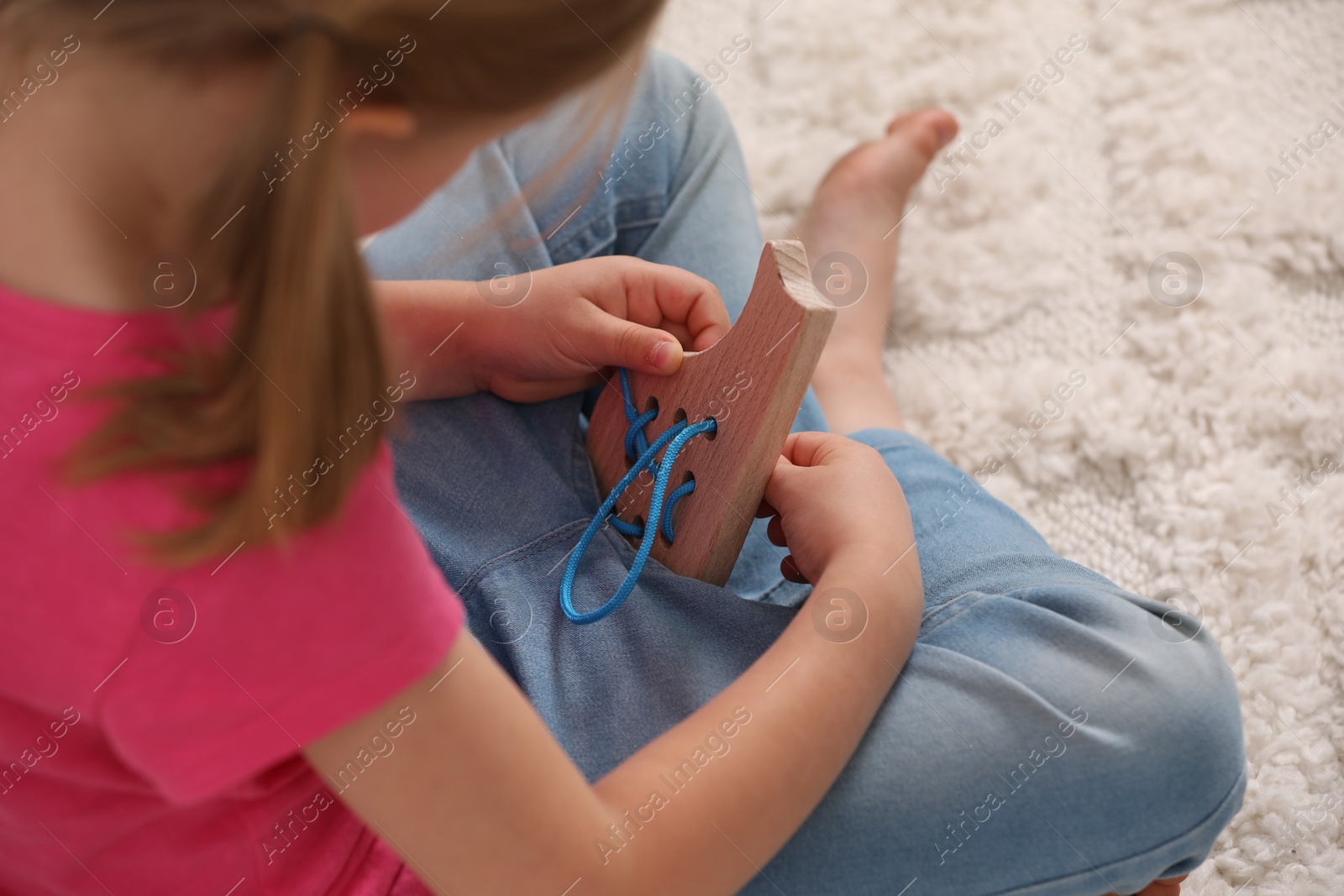 Photo of Little girl playing with wooden lacing toy on carpet indoors, closeup