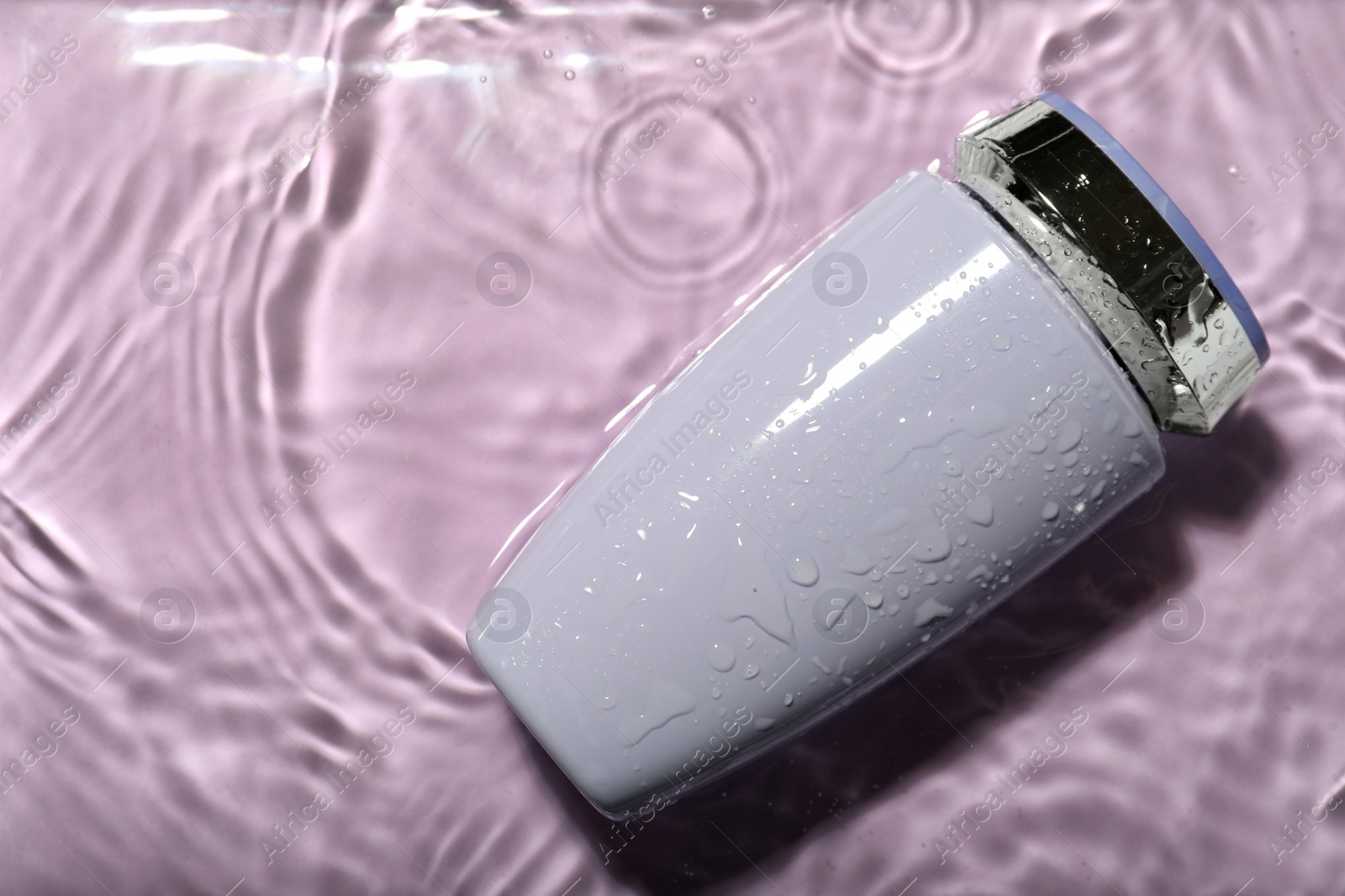 Photo of Bottle of hair care cosmetic product in water on violet background, top view. Space for text