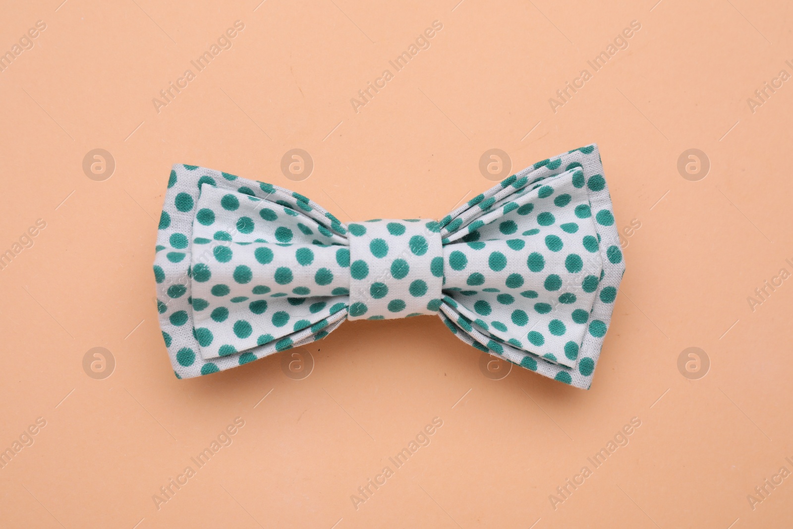 Photo of Stylish white bow tie with green polka dot pattern on pale orange background, top view