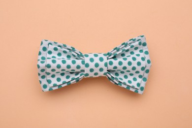 Stylish white bow tie with green polka dot pattern on pale orange background, top view