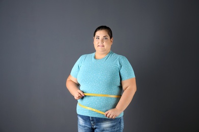 Overweight woman with measuring tape on gray background