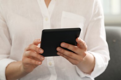 Young woman using e-book reader at home, closeup