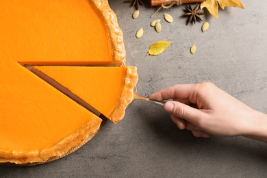 Woman with piece of fresh delicious homemade pumpkin pie on table, top view