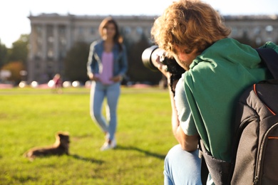 Male photographer taking photo of young woman with professional camera on grass outdoors