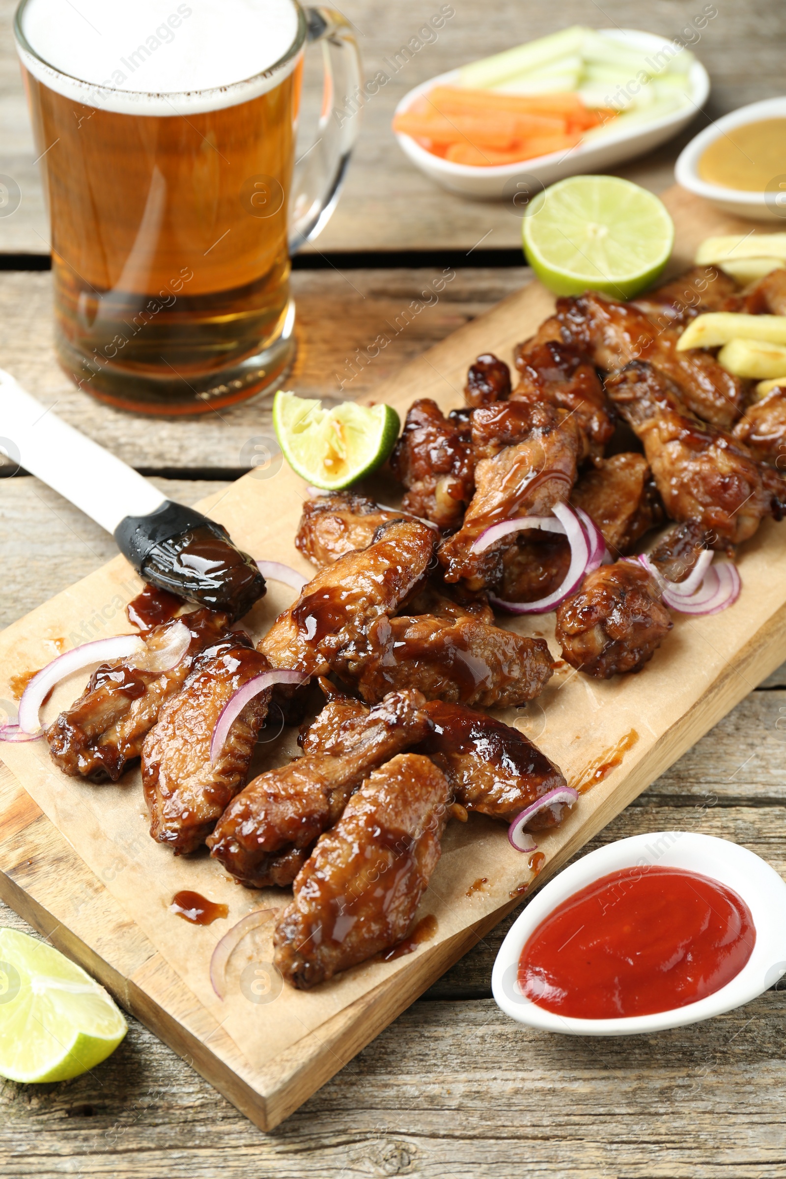 Photo of Tasty roasted chicken wings, mug of beer and sauce on wooden table
