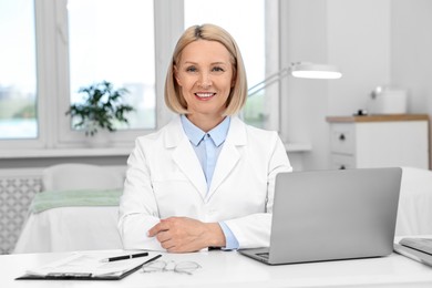 Portrait of happy dermatologist at white table in clinic