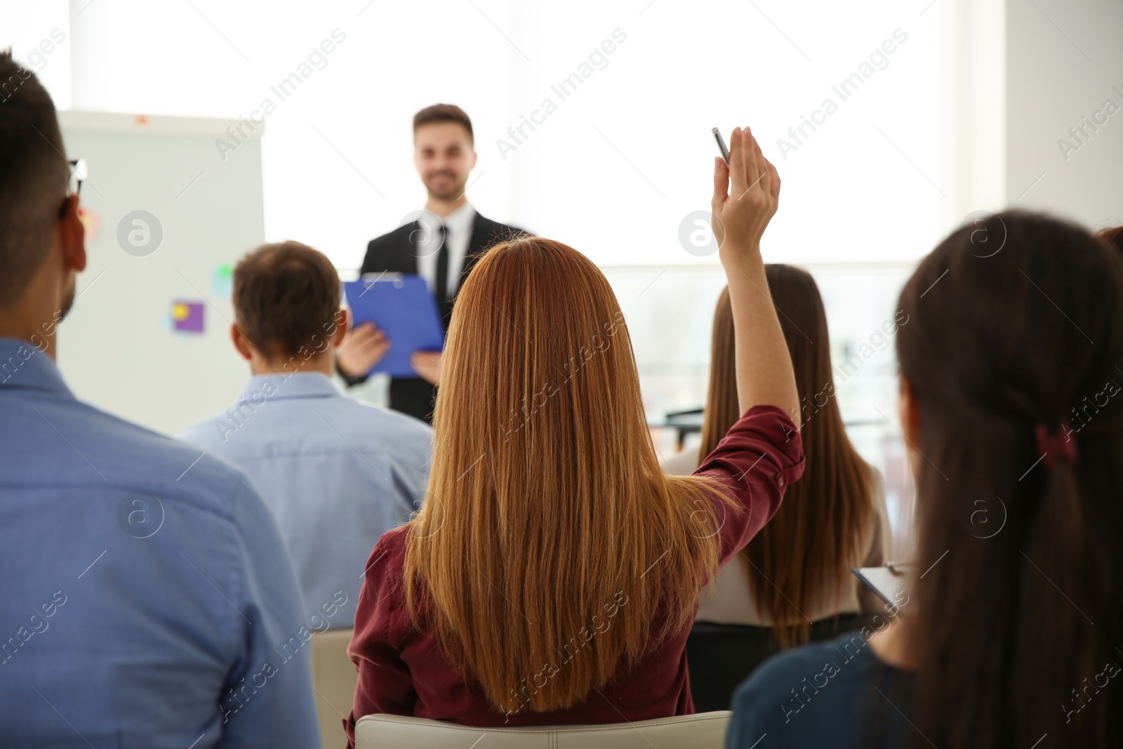 Photo of Young woman raising hand to ask question at business training indoors, back view