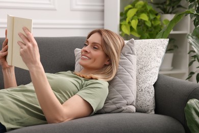 Photo of Woman reading book on sofa in room with houseplants