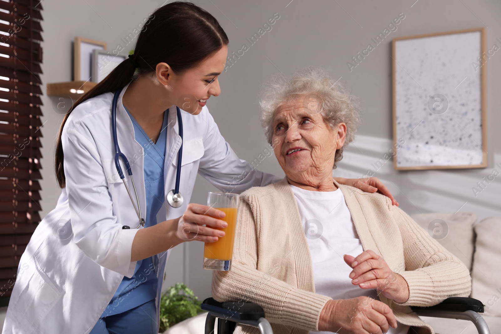 Photo of Young caregiver giving drink to senior woman in room Home health care service