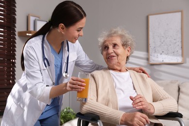 Photo of Young caregiver giving drink to senior woman in room Home health care service