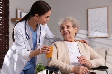 Young caregiver giving drink to senior woman in room Home health care service