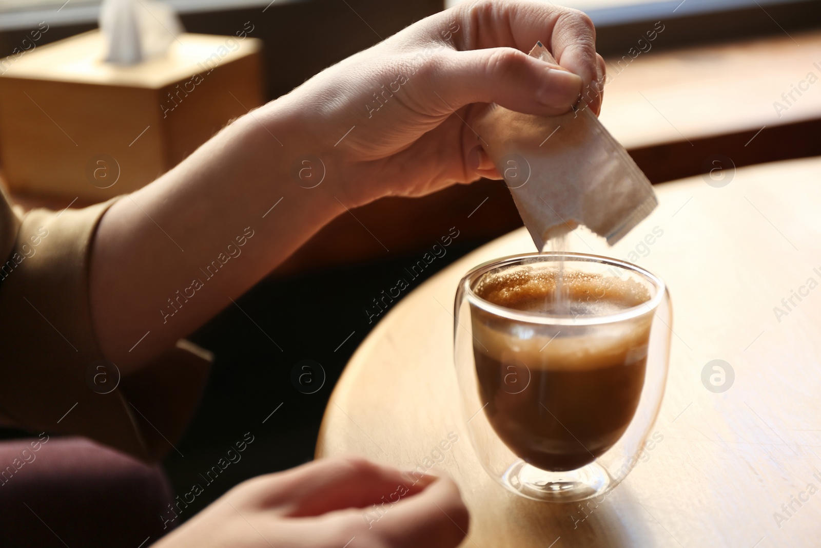 Photo of Woman adding sugar to aromatic coffee at table in cafe, closeup