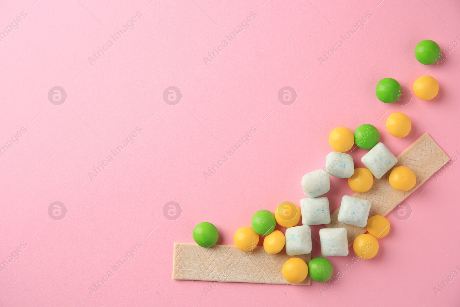 Photo of Different tasty chewing gums on pink background, flat lay. Space for text