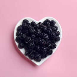 Heart shaped plate of ripe blackberries on pink background, top view