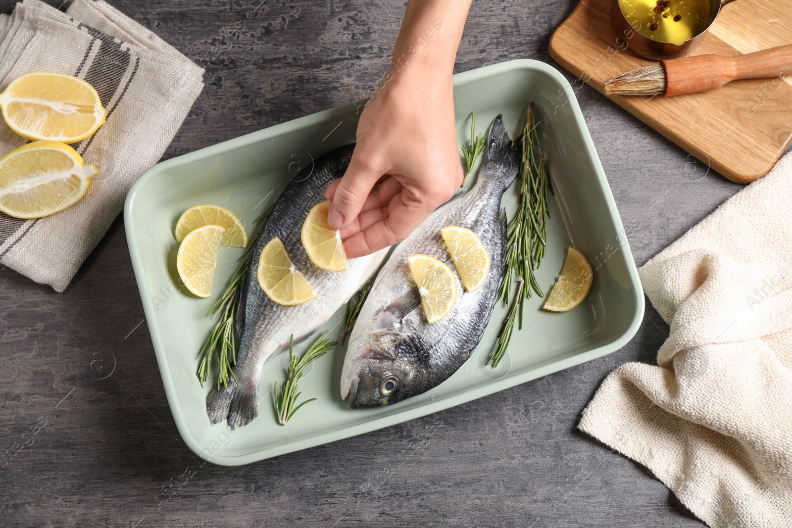 Photo of Woman adding lemon to raw dorada fish on grey table, top view