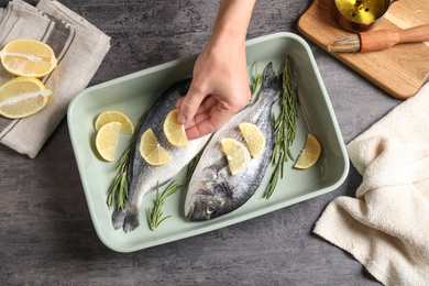 Photo of Woman adding lemon to raw dorada fish on grey table, top view