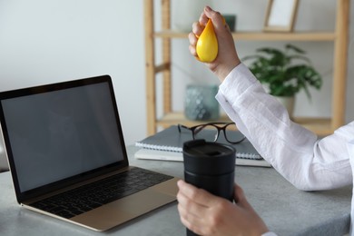 Woman squeezing antistress ball at workplace, closeup