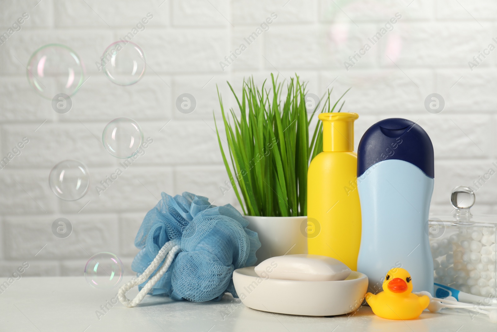 Photo of Different baby bath accessories and cosmetic products on white table against brick wall