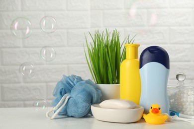 Different baby bath accessories and cosmetic products on white table against brick wall