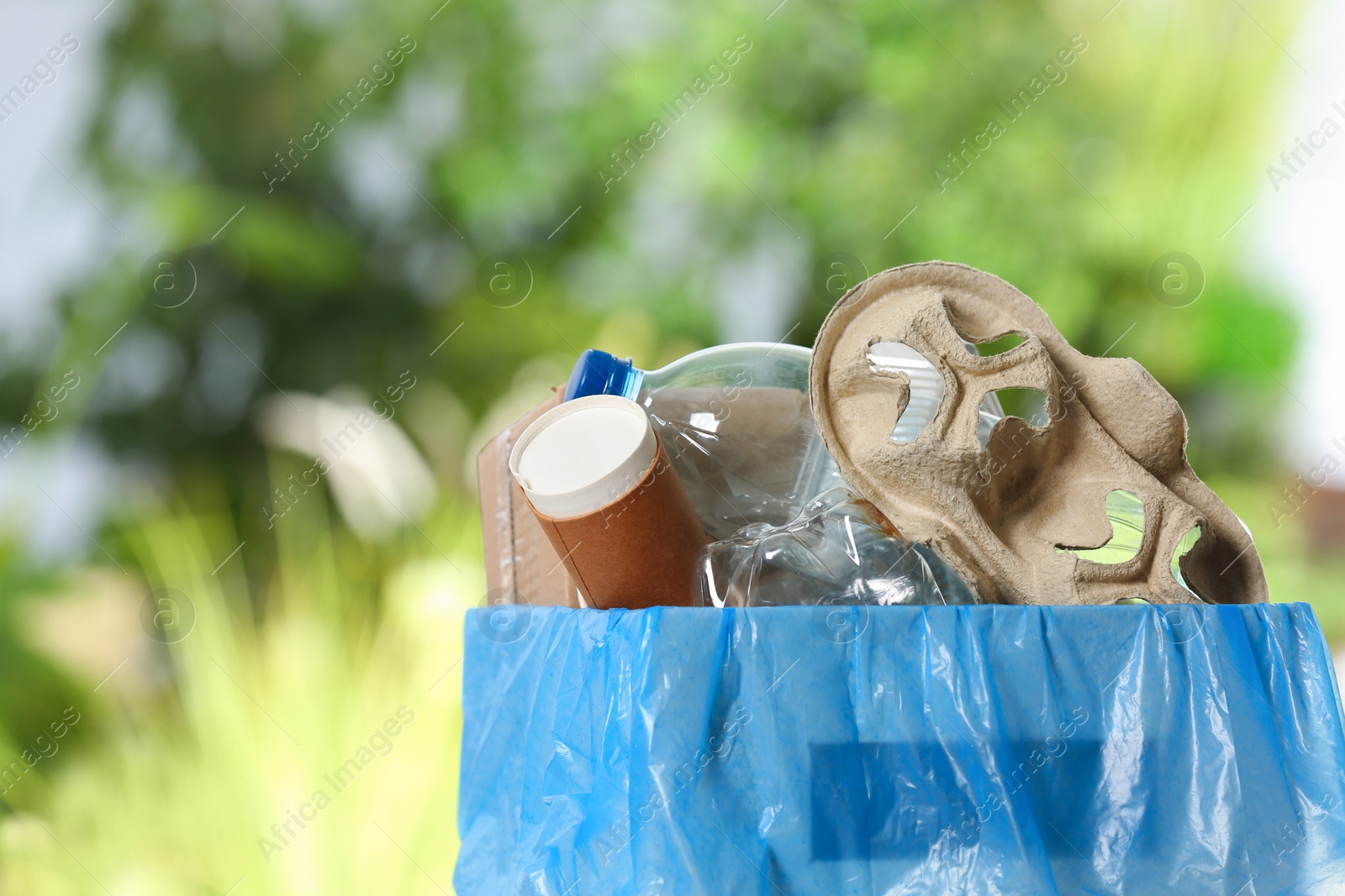 Photo of Trash bin with garbage on blurred background, space for text. Recycling problem