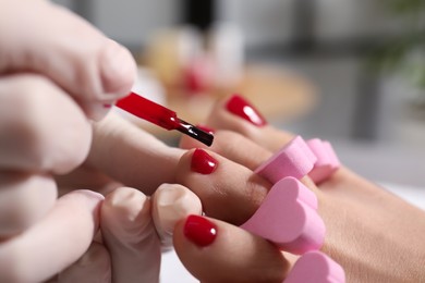 Photo of Pedicurist painting client`s toenails with red polish in beauty salon, closeup