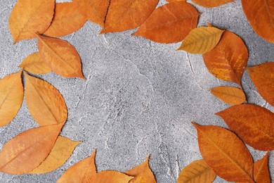 Photo of Frame of beautiful orange leaves on grey textured table, flat lay. Space for text