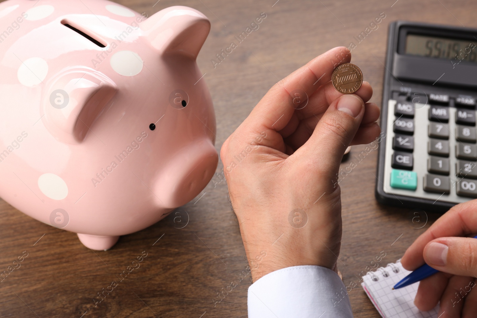 Photo of Budget planning. Businessman with coin and piggy bank calculating at wooden table, closeup