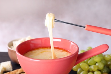 Dipping bread into pot with cheese fondue, closeup