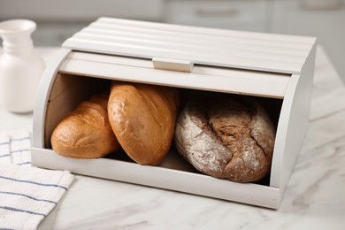 Photo of Wooden bread basket with freshly baked loaves on white marble table in kitchen