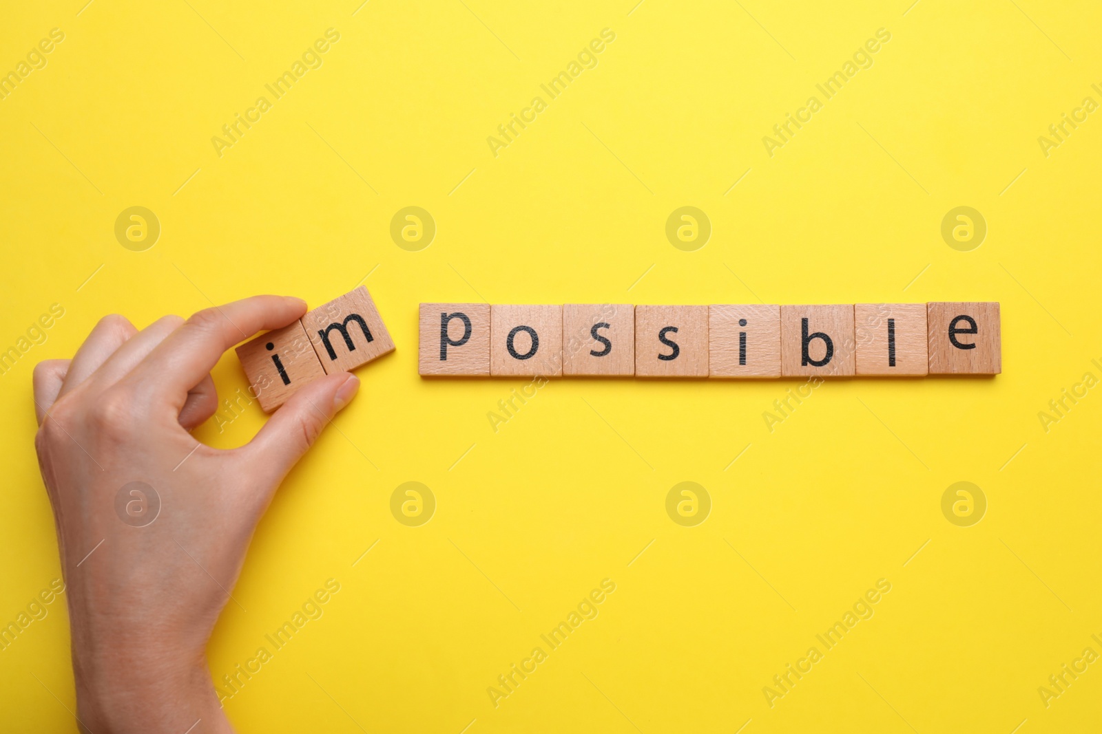 Photo of Motivation concept. Woman changing word from Impossible into Possible by removing wooden squares on yellow background, top view