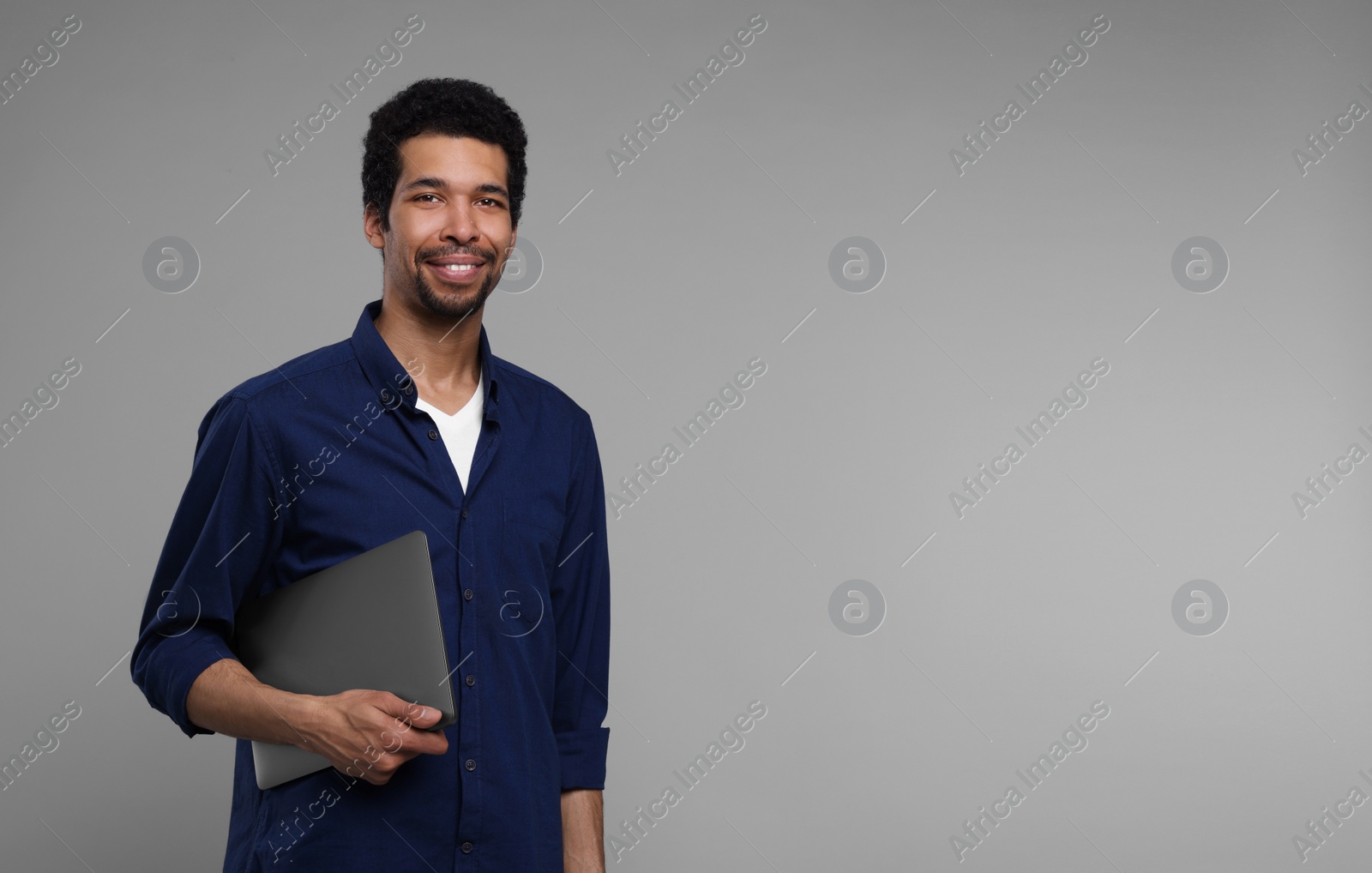 Photo of Happy man with laptop on grey background. Space for text