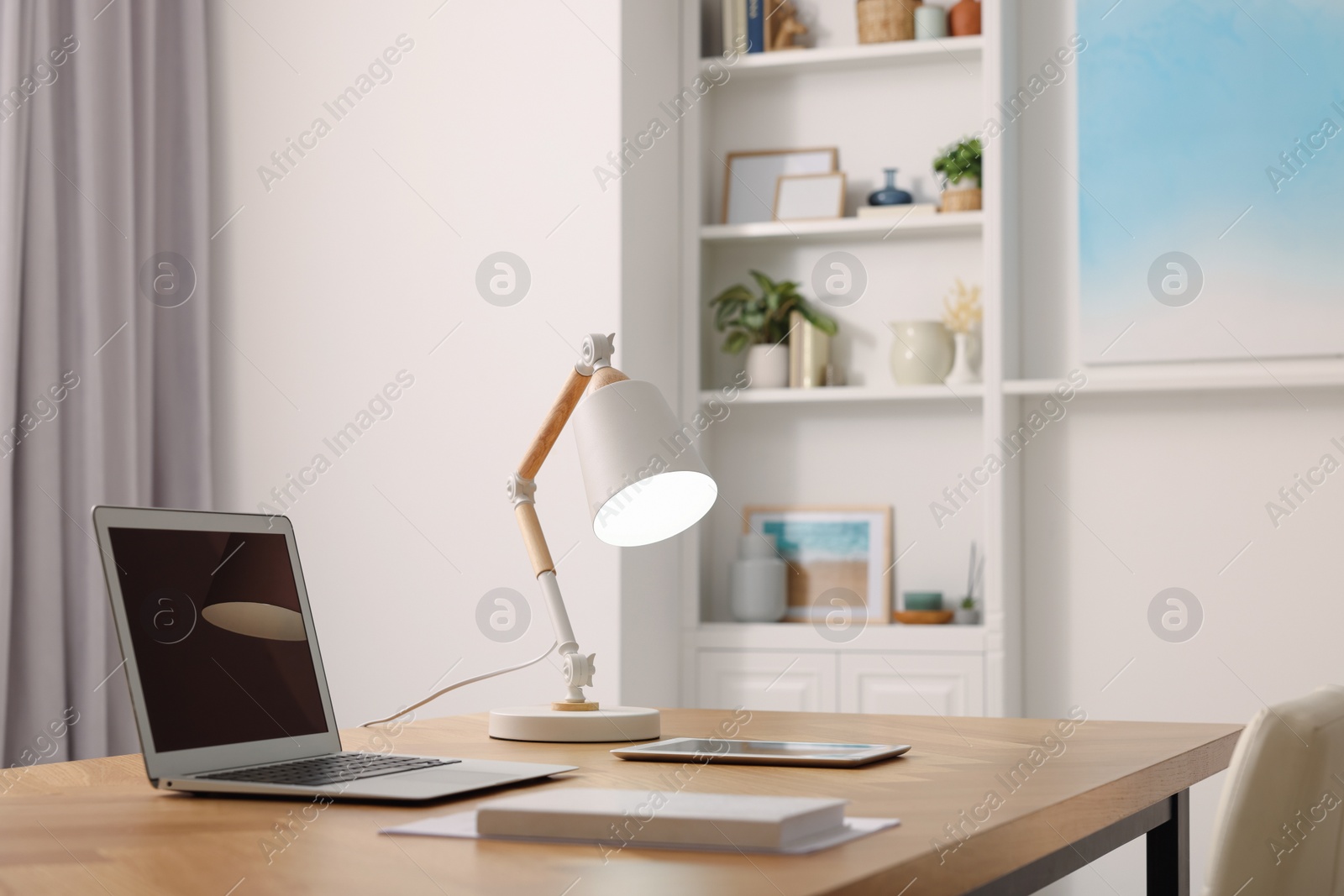 Photo of Interior design. Cosy workplace with laptop and lamp on wooden table