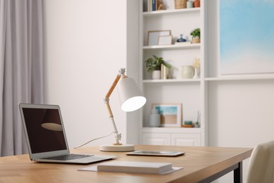 Photo of Interior design. Cosy workplace with laptop and lamp on wooden table