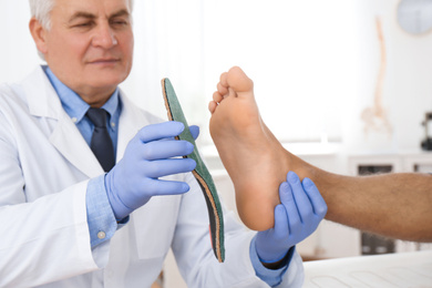 Photo of Male orthopedist fitting insole on patient's foot in clinic