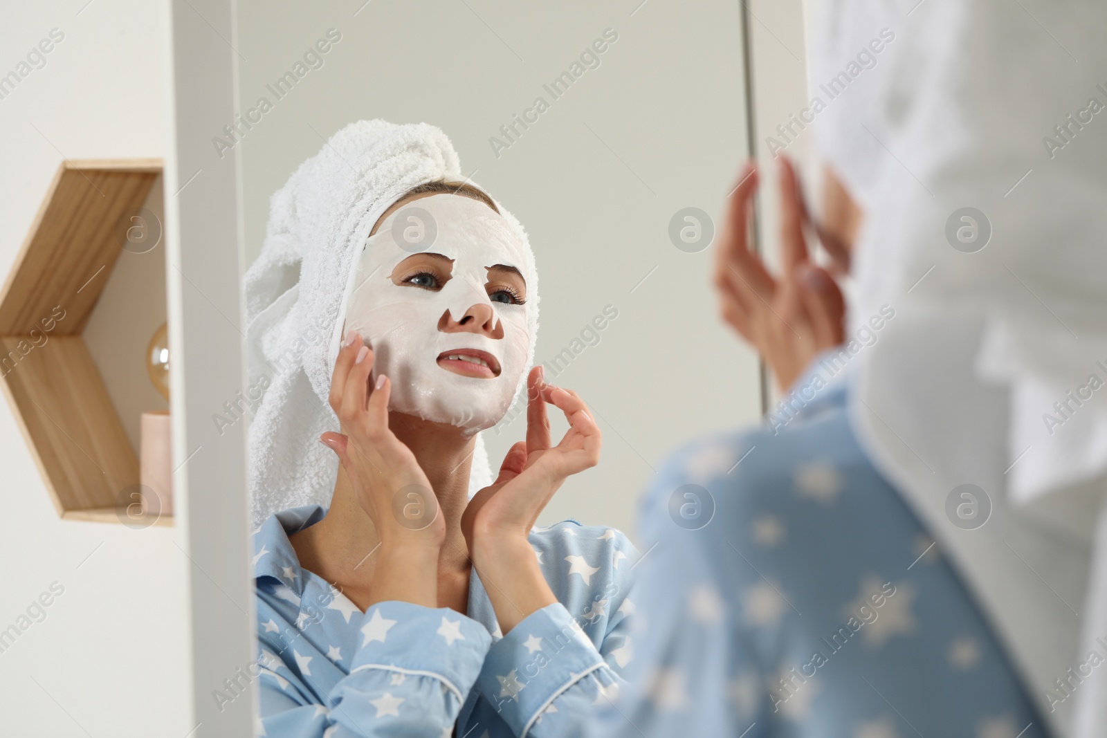 Photo of Young woman with face mask looking into mirror indoors. Spa treatments