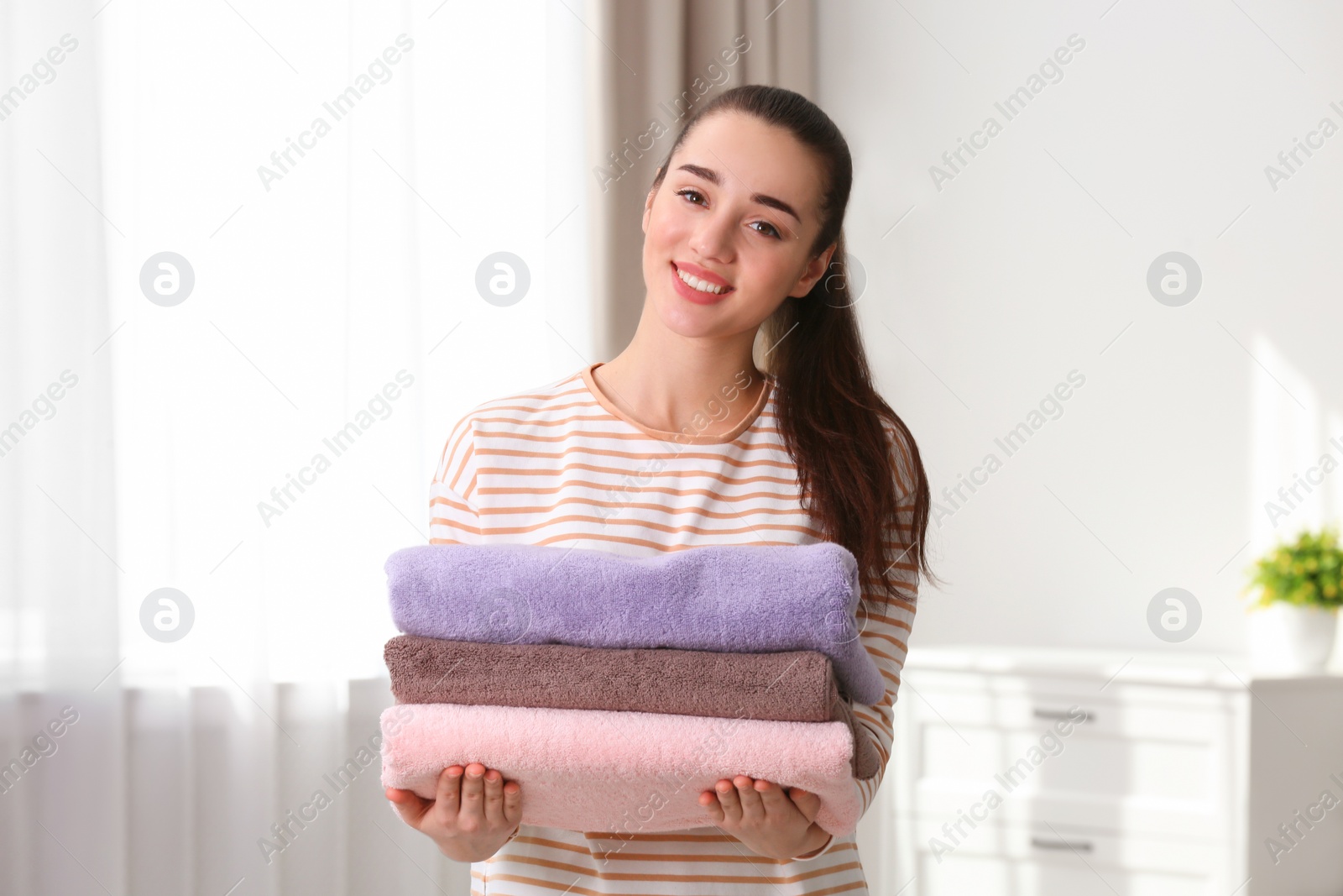 Photo of Happy young woman holding clean laundry at home