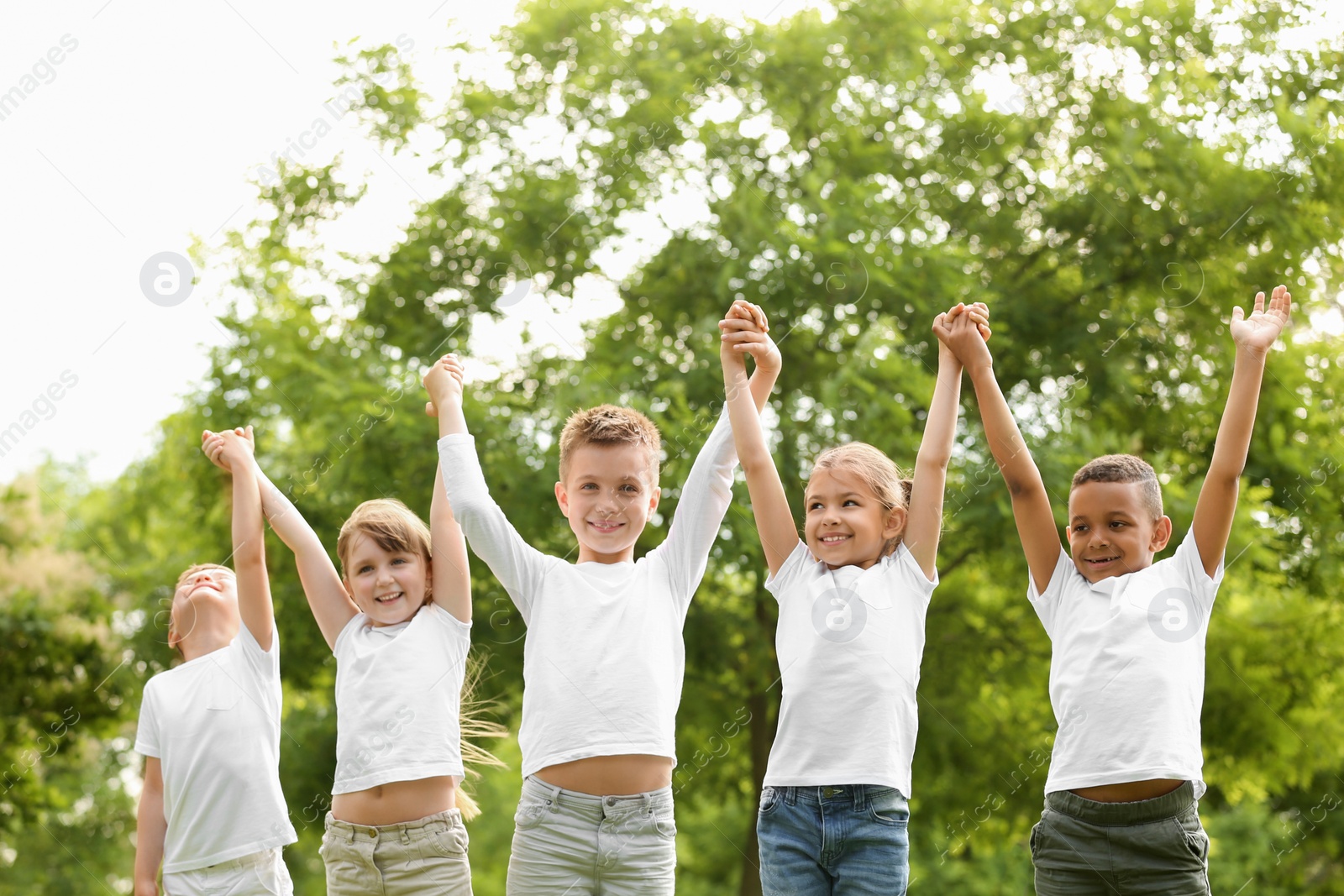 Photo of Group of children holding hands up in park. Volunteer project