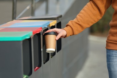 Photo of Man throwing coffee cup into sorting bin outdoors, closeup