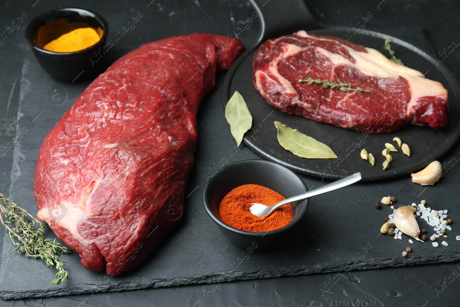 Photo of Pieces of raw beef meat and spices on black table