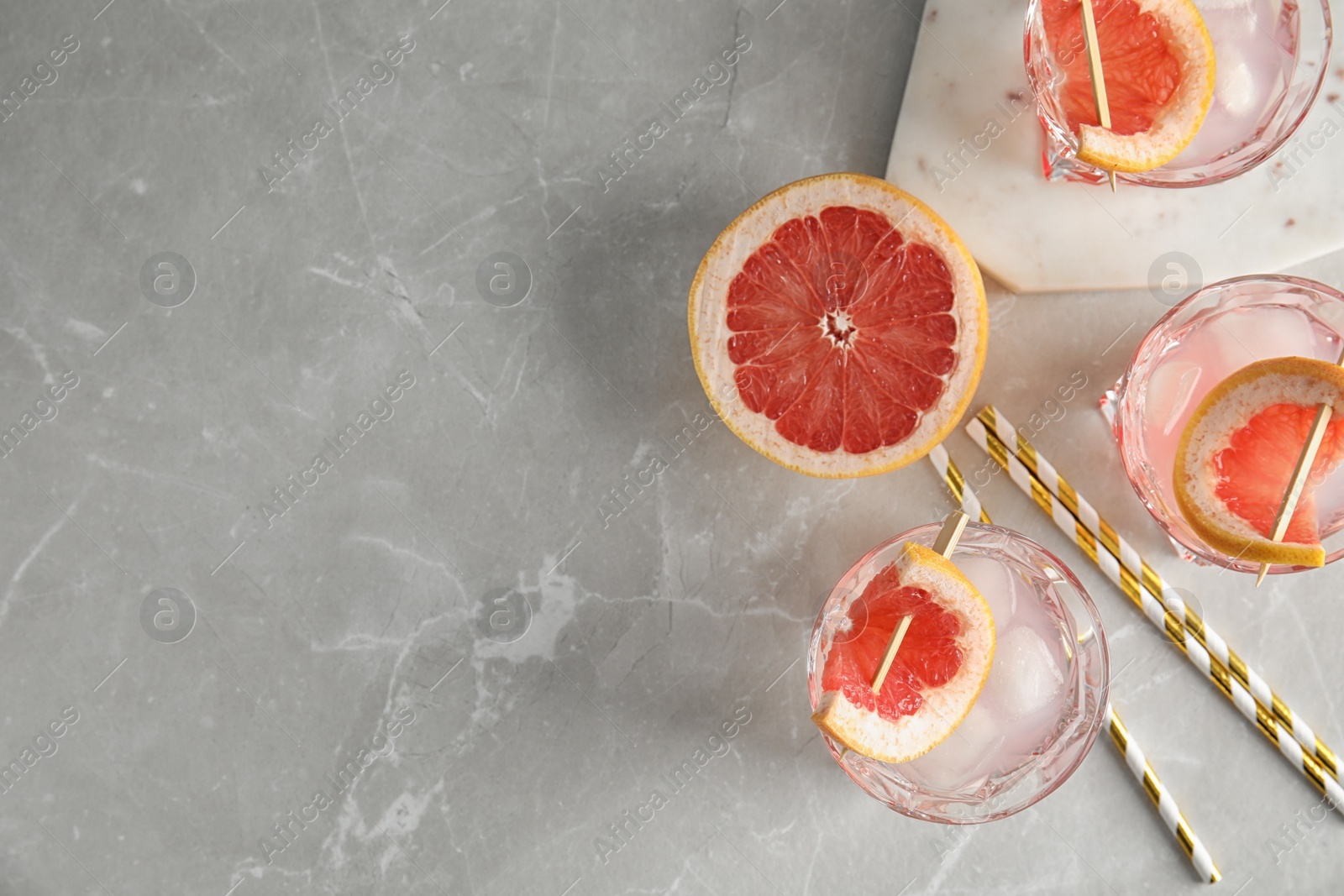 Photo of Flat lay composition with glasses of grapefruit cocktails on grey table. Space for text