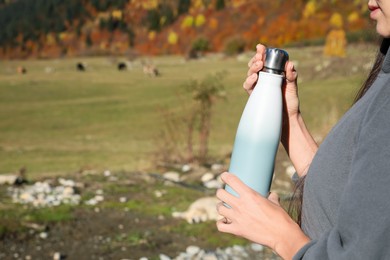 Photo of Woman holding thermo bottle with drink in mountains on sunny day. Space for text